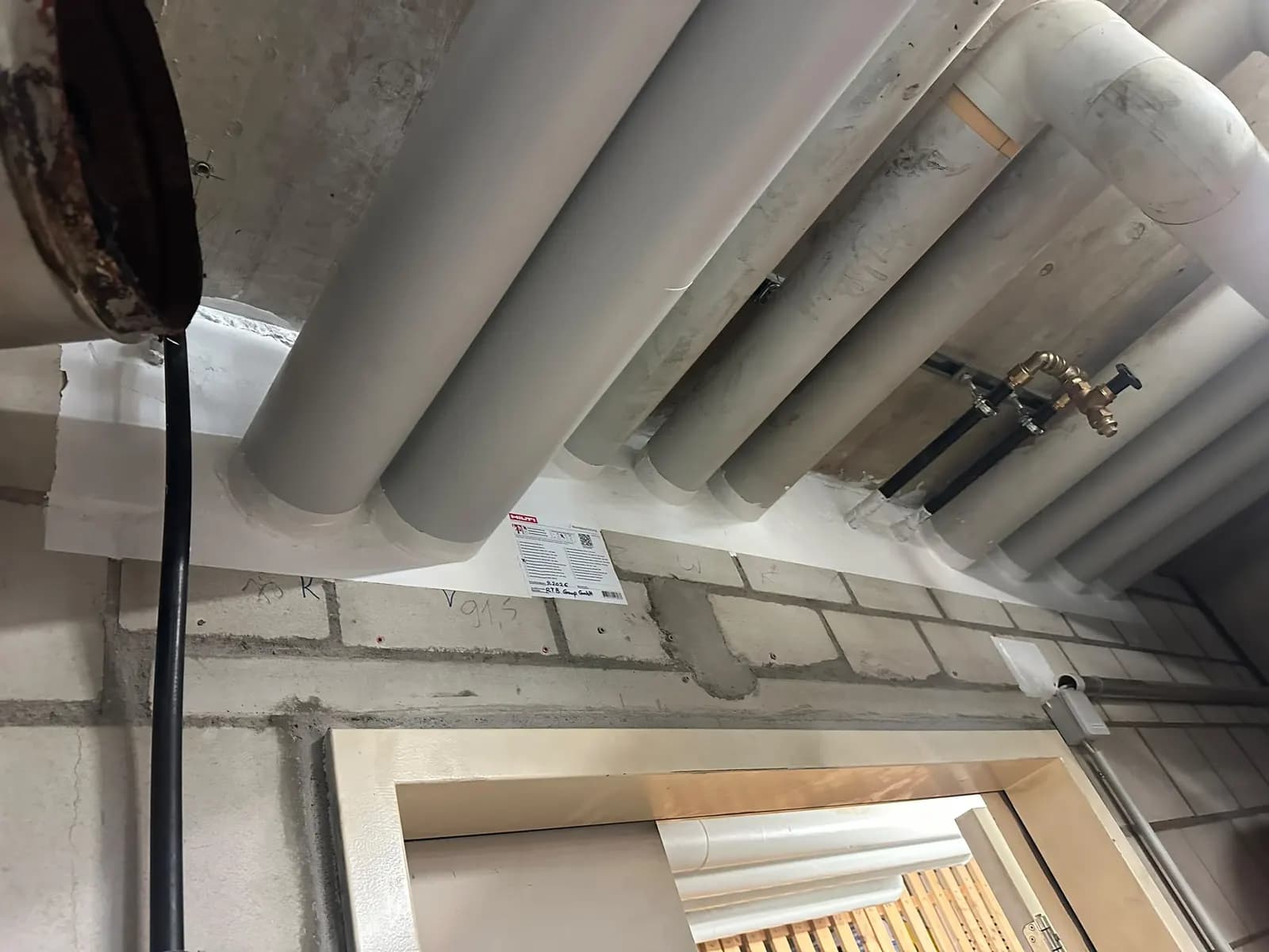 Mehrere gedämmte Rohrleitungen durchstossen eine Wand über einer Tür, die Durchführung ist flächig abgeschottet und beschildert